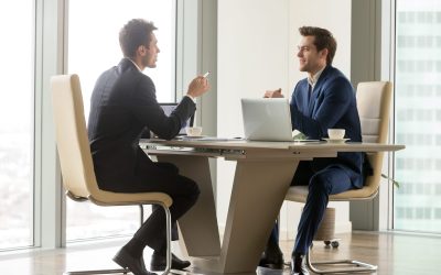 Two handsome businessmen sitting in comfortable chairs at desk with laptops in meeting room. CEO making important negotiation about companies partnership or corporate merger. Financiers planning deal